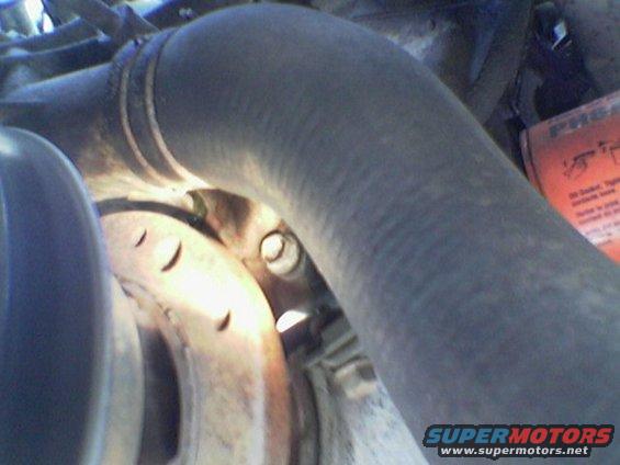 Close-up of a thick rubber hose curving over a metal pulley with visible bolt heads