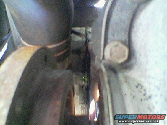 Close-up of engine bay hoses and metal parts. A bolt is visible on the right