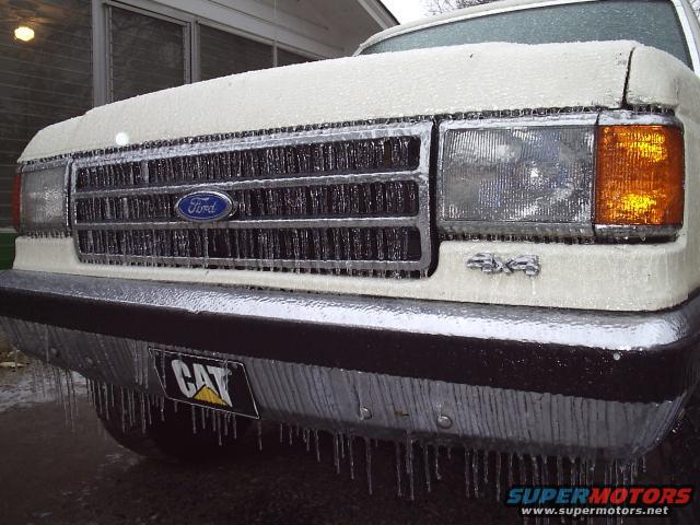 Front of a white Ford truck with ice covering the grille and headlights. A CAT license plate frame is visible