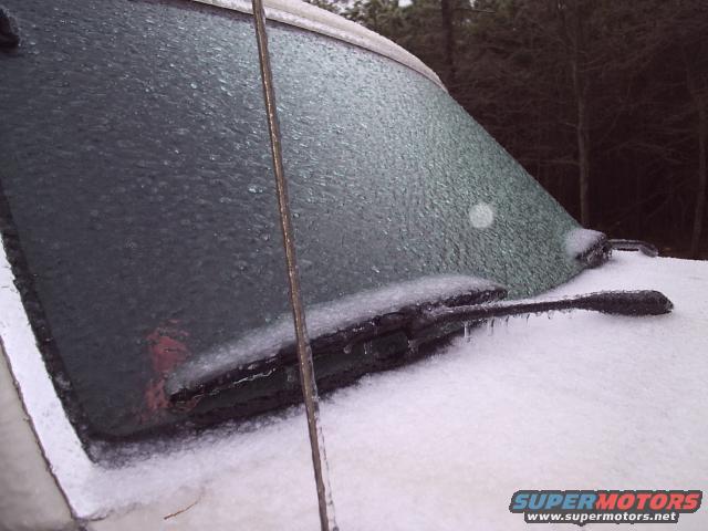 Windshield and wiper blades of a vehicle encased in ice, with snow on the hood