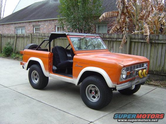 Orange first-generation Ford Bronco with white trim and aftermarket wheels, soft top removed