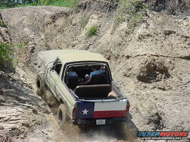 1978 Ford Bronco driving up a dirt hill, Texas flag decal on tailgate