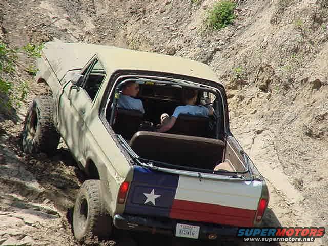 Off-roading in a 1978 Ford Bronco climbing a dirt hill with two people inside
