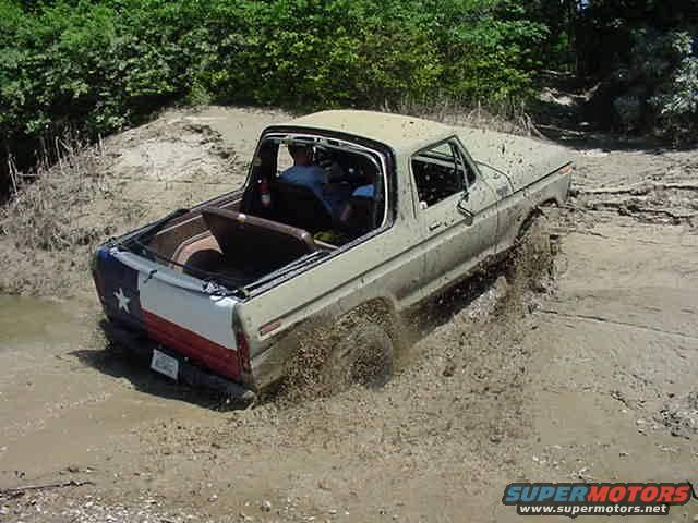 Tan 1978 Ford Bronco with Texas flag decal on rear, stuck in mud