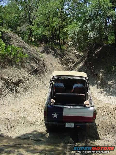 Tan 1978 Ford Bronco with Texas flag tailgate driving on a dirt path