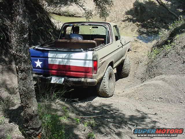 1978 Ford Bronco with Texas flag painted on the tailgate driving on a dirt trail