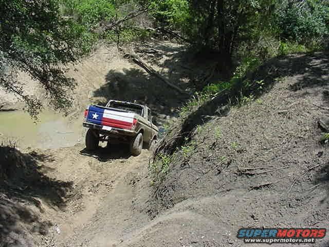 Brown pickup truck with Texas flag tailgate driving on dirt hill