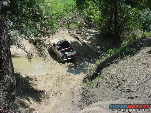 Off-road vehicle struggling on a muddy hill near water
