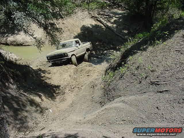 1978 Ford Bronco driving down a muddy hill next to a creek