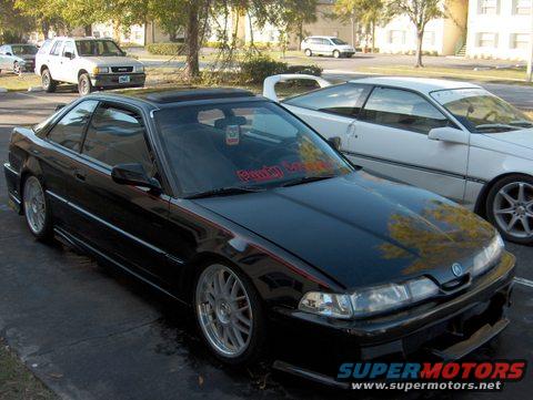 Black 1990 Acura Integra coupe with aftermarket wheels, parked next to a white car