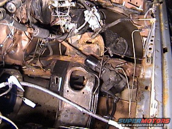 Engine bay showing rusted metal, hoses, and wiring. Some components are covered in grime