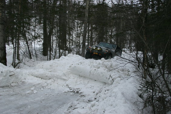 Jeep TJ driving through a deep snow drift on a wooded trail. It's a 2003 Jeep TJ