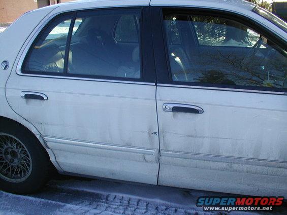 White sedan side view, dent on rear door, chrome trim, wire wheel