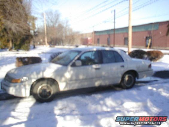White sedan parked on a snowy street, side view