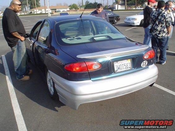 Dark blue sedan with silver lower body kit and a spoiler. License plate is 3WOT583. GB sticker on rear