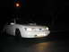 1995 Ford Taurus - This white 1995 Ford Taurus is captured in a three-quarter front view at night, illuminated by its headlights and additional lower lights.