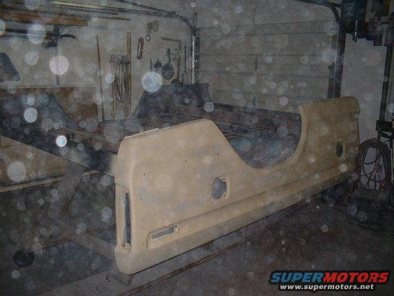 Tan truck bed side panel with circular cutouts, resting on a stand in a garage