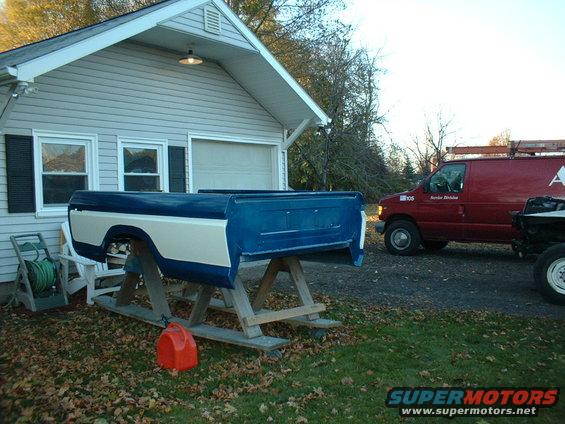 Blue and white pickup truck bed on sawhorses, red van in background