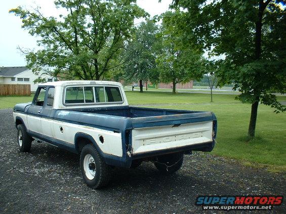1978 Ford F-250 pickup truck, two-tone white and blue, parked on gravel with trees and a building in the background