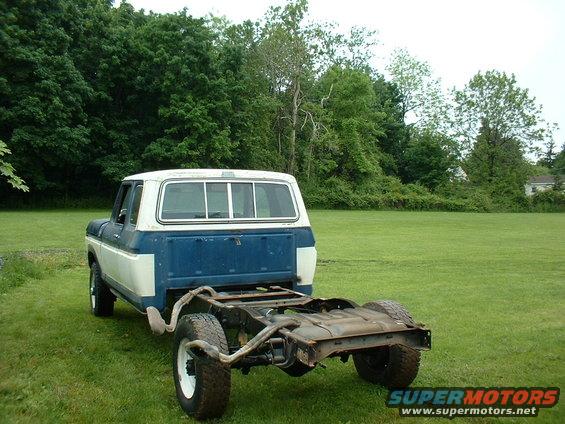 Blue and white Ford F-250 truck chassis with rear wheels visible, parked on grass