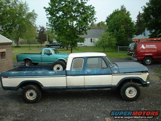 1978 Ford F-250 crew cab pickup truck, blue and white, parked next to a teal pickup truck and a red van