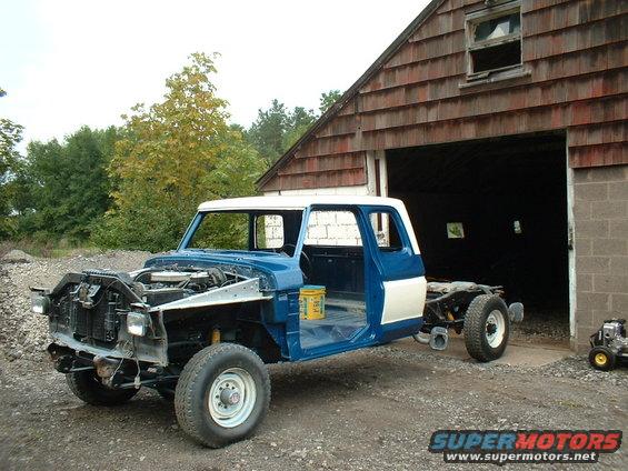 Ford F-Series truck body on a chassis, missing front clip and bed, parked outside a barn