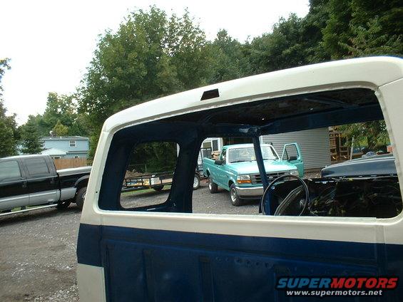 View through an open pickup truck cab shows a teal pickup truck with doors open and a black pickup truck in the background