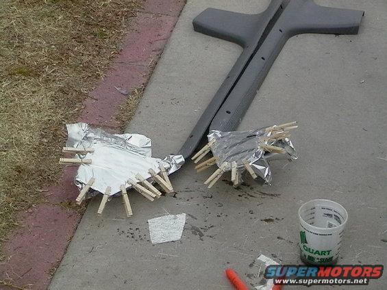 Two car parts wrapped in foil and secured with clothespins sit on concrete next to a gray trim piece
