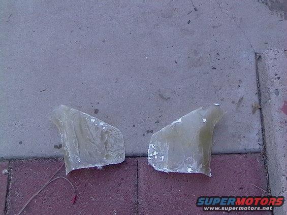 Two unfinished fiberglass automotive parts on a paved surface