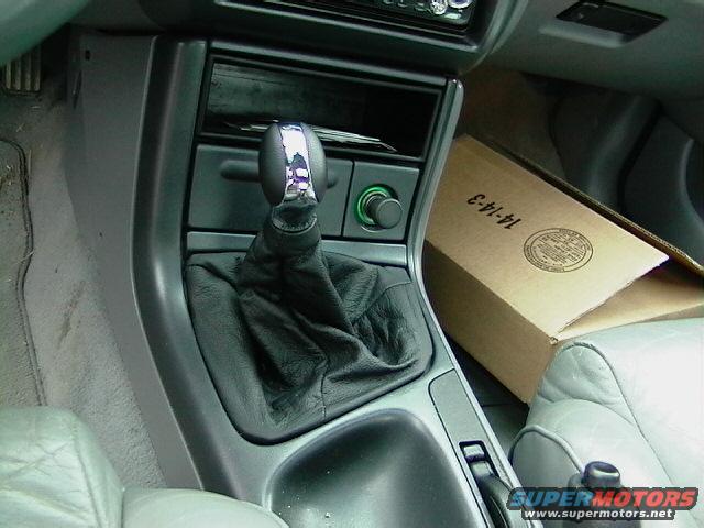 Car interior showing a leather-booted gear shifter, center console, and a cardboard box with text '14-14-3'
