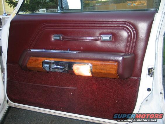 Maroon car door panel with wood trim, chrome handle, and interior light