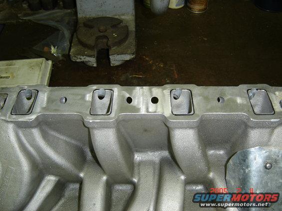 Bare aluminum V8 intake manifold on a workbench, machined port flange facing up