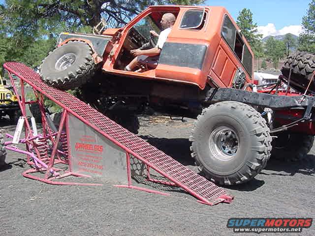 Orange off-road truck with large tires on a red ramp. A person is in the driver's seat