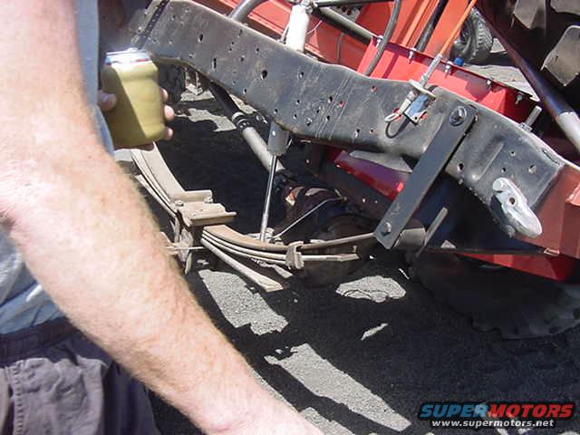 Leaf spring suspension on a vehicle frame, with a hand holding a can