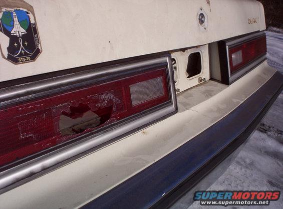 Close-up of a car's rear bumper and taillight, with a broken taillight lens and a STS-70 space shuttle sticker