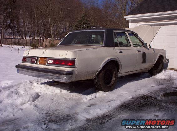 White sedan with black roof parked in snow, rear view. License plate reads 687-06
