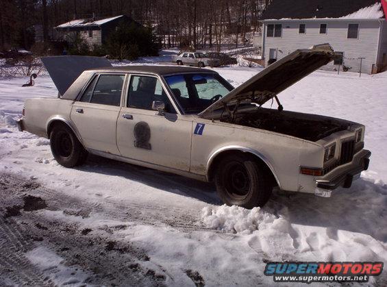 White sedan with hood and trunk open, parked in snow. Has a shield emblem and number 7 on the door