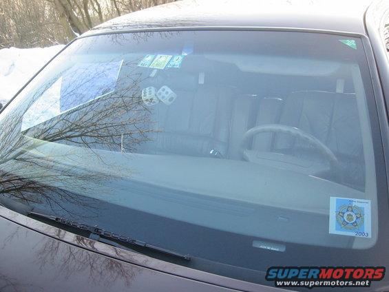 Car interior showing dashboard, steering wheel, and seats through the windshield. Dice hanging from rearview mirror