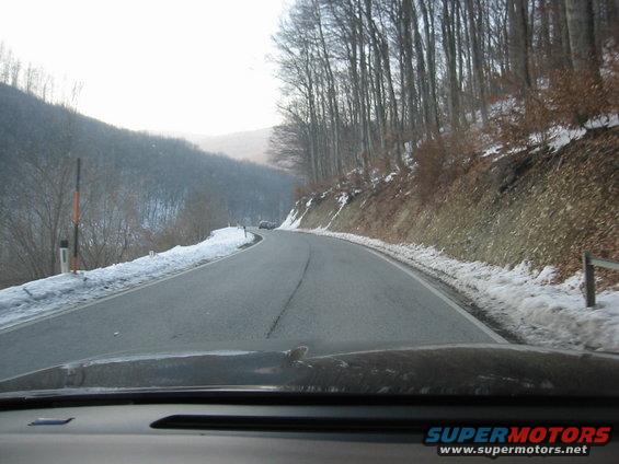 Driving on a snowy road through a forest with bare trees