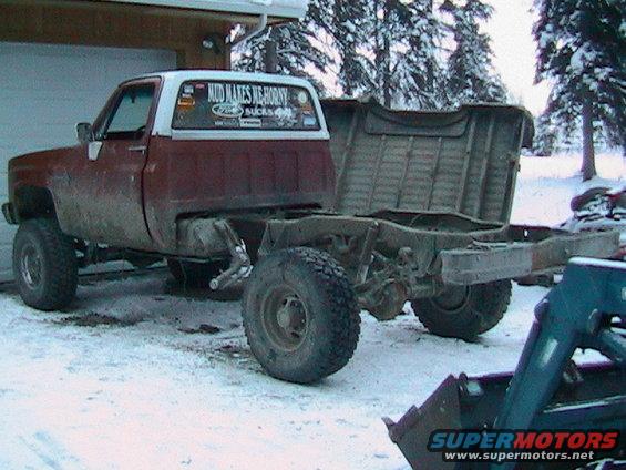 Red and white pickup truck chassis with missing bed, parked in snow