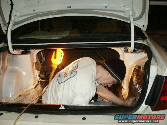 Guy working in car trunk, installing sound dampening material. Yellow work light is on