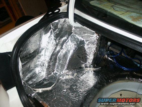 Car trunk interior with silver sound dampening material and blue wires visible