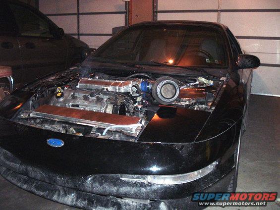 Black car with hood open, showing engine and turbocharger. Ford logo visible on front