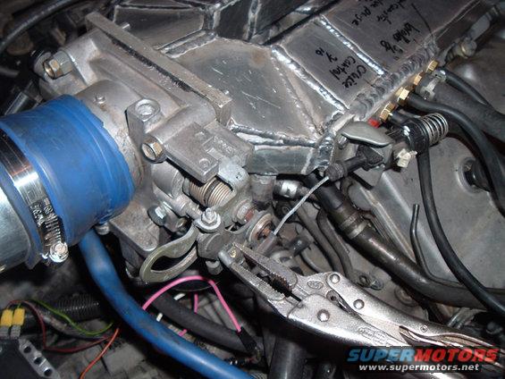 Custom intake manifold with throttle body, blue hose, and vise grips on cable