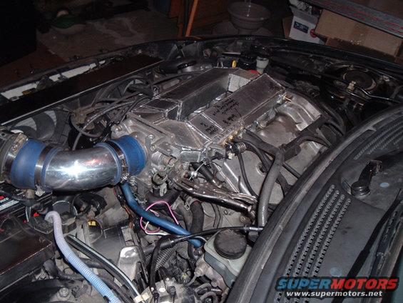 Engine bay showing custom intake manifold and piping. Some writing is visible on the manifold