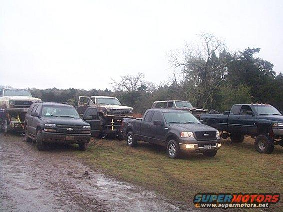 Several trucks and SUVs parked on a muddy field under an overcast sky