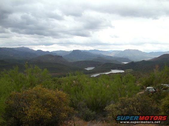 Mountainous terrain with two lakes under a cloudy sky; a vehicle is partially visible on the right