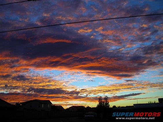 Sunset clouds over houses with a faint vehicle in the distance