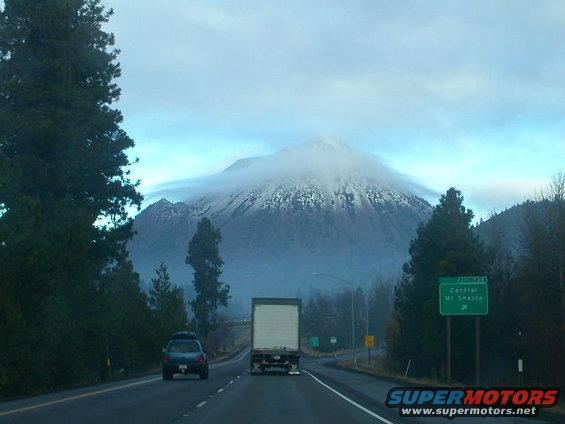 Highway driving towards a snow-capped mountain, with a truck and car on the road