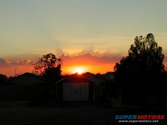 Sunset over suburban houses and a garage with Supermotors.net logo